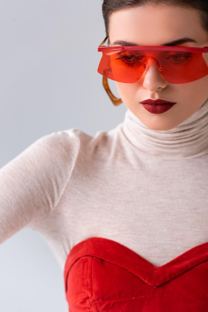 όμορφο, κομψό κορίτσι με κόκκινα γυαλιά ηλίου ποζάρουν απομονωμένο σε γκρι - Φωτογραφία, εικόνα