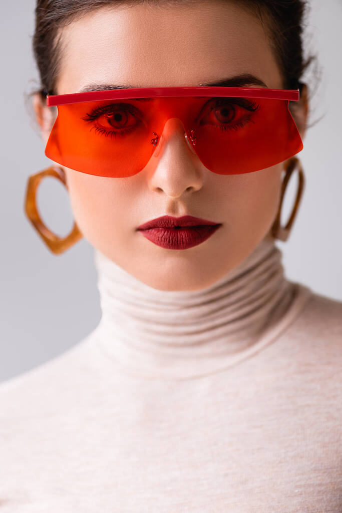 Ritratto di bella donna in occhiali da sole rossi guardando la macchina fotografica isolata su grigio  - Foto, immagini