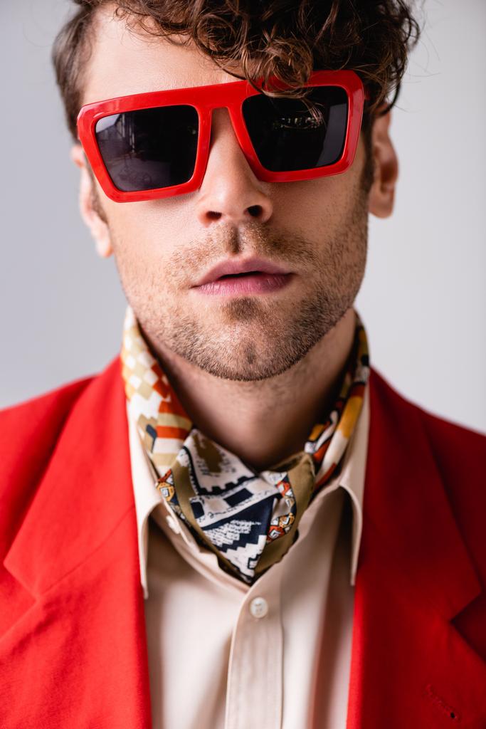 Porträt eines gutaussehenden Mannes mit Sonnenbrille, der isoliert in die Kamera auf grau blickt  - Foto, Bild