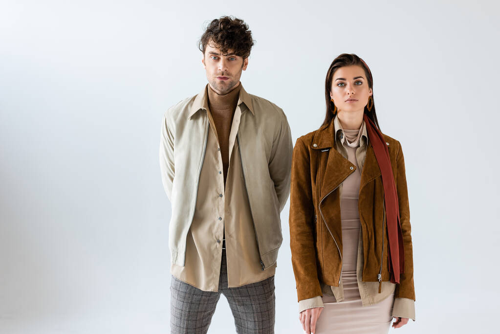 Stylish woman and man in autumn outfit looking at camera and standing together on grey - Photo, Image