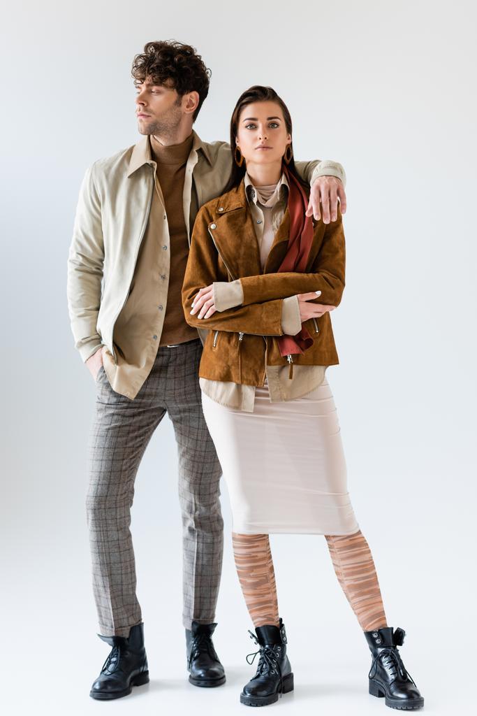 Volledige weergave van stijlvolle man met de hand in zak kijken weg, terwijl omarmen aantrekkelijke vrouw in de buurt staan op grijs - Foto, afbeelding