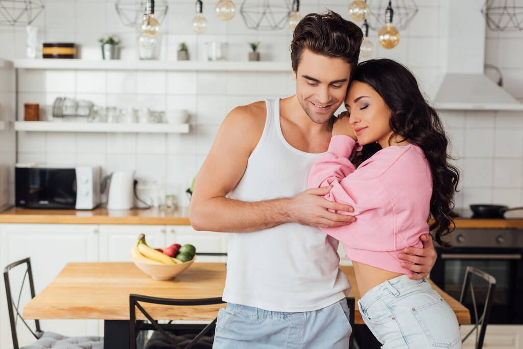 Улыбающийся мужчина обнимает красивую девушку на кухне  - Фото, изображение