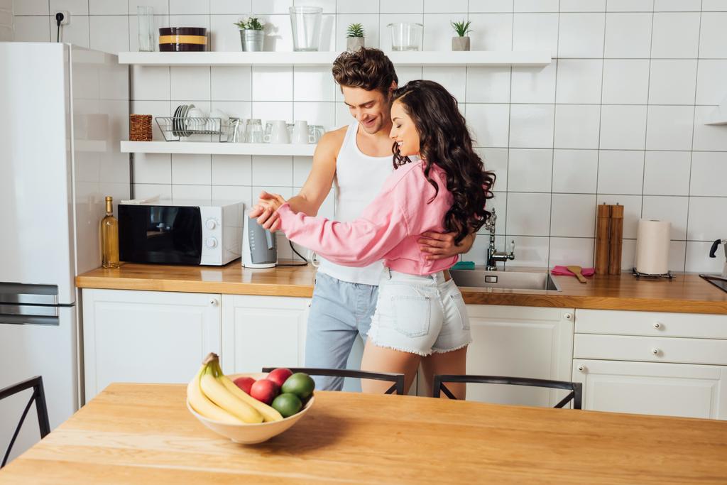 キッチンで踊りながら笑顔の若いカップルの選択的な焦点  - 写真・画像
