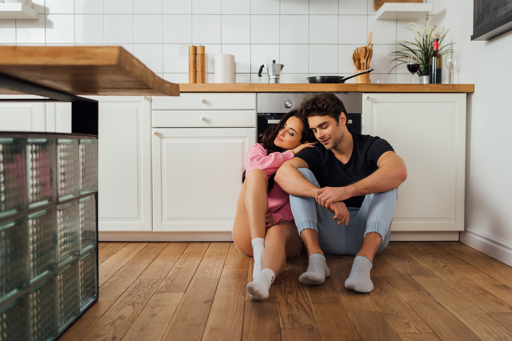 Selective focus of beautiful woman hugging boyfriend with closed eyes on kitchen floor  - Photo, Image