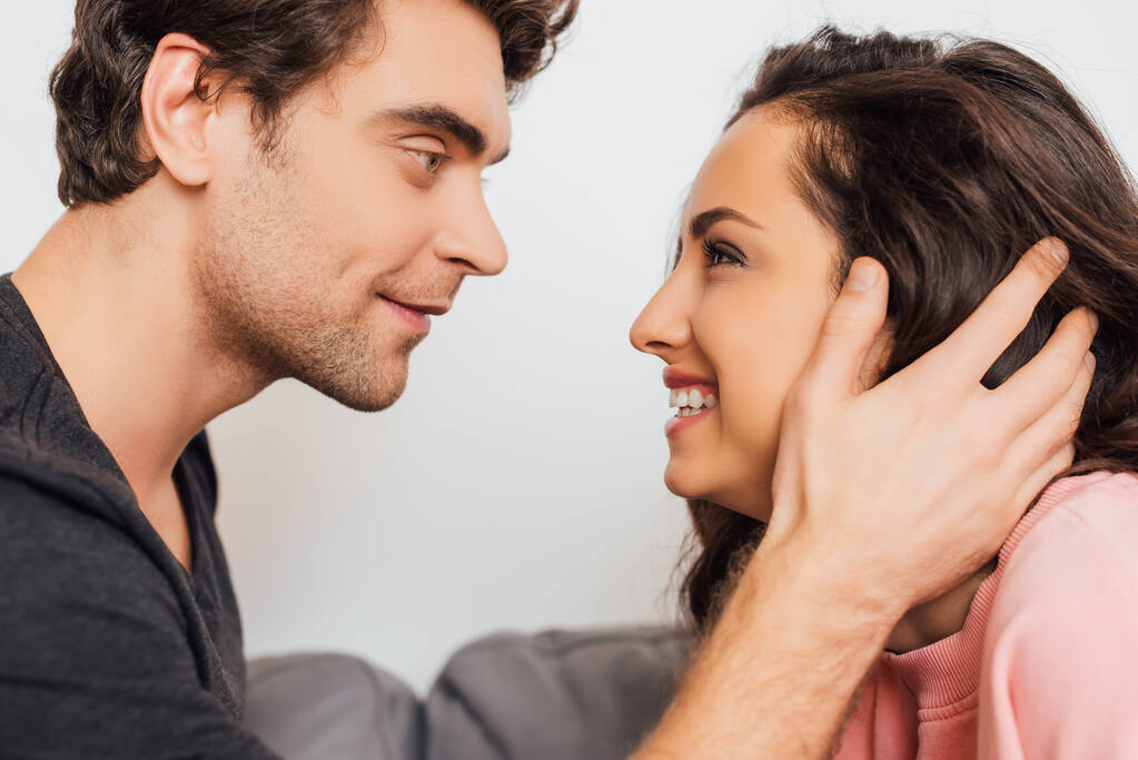 Schöner Mann berührt Haare lächelnder Freundin auf Couch isoliert auf grau  - Foto, Bild