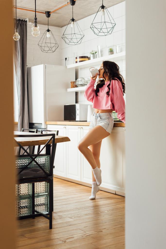 Selective focus of beautiful brunette woman drinking coffee in kitchen  - Photo, Image