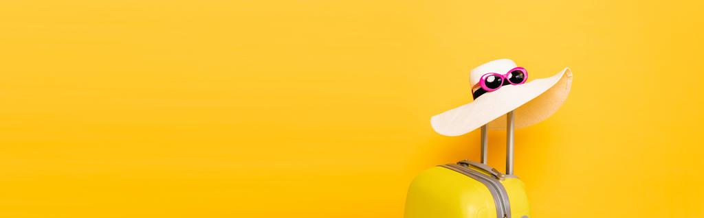 chapeau de soleil et lunettes de soleil sur la valise poignée sur fond jaune, vue panoramique - Photo, image