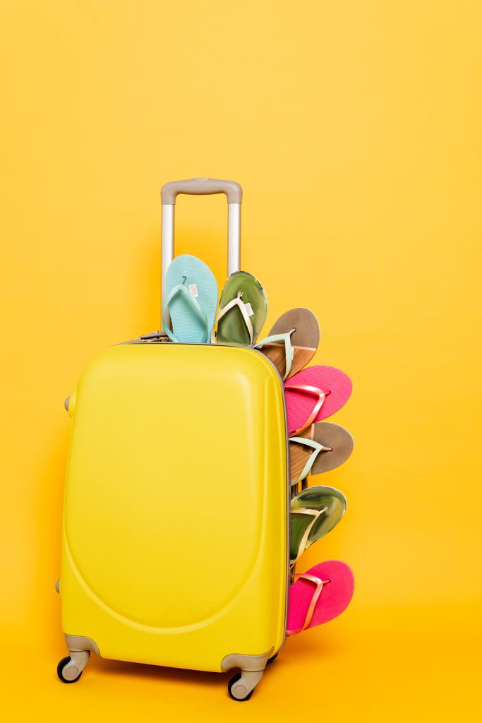 ταξιδιωτική τσάντα με πολύχρωμες σαγιονάρες σε κίτρινο φόντο - Φωτογραφία, εικόνα