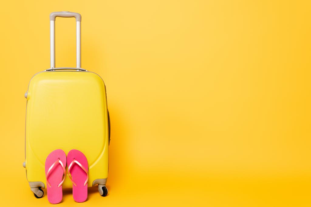utazási táska rózsaszín flip flops elszigetelt sárga háttér - Fotó, kép