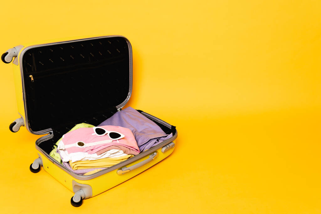 Sarı arka planda yaz kıyafetleri ve aksesuarları olan seyahat çantalarını aç - Fotoğraf, Görsel