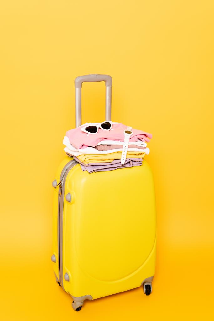 travel bag with summer clothes and accessories isolated on yellow - Photo, Image