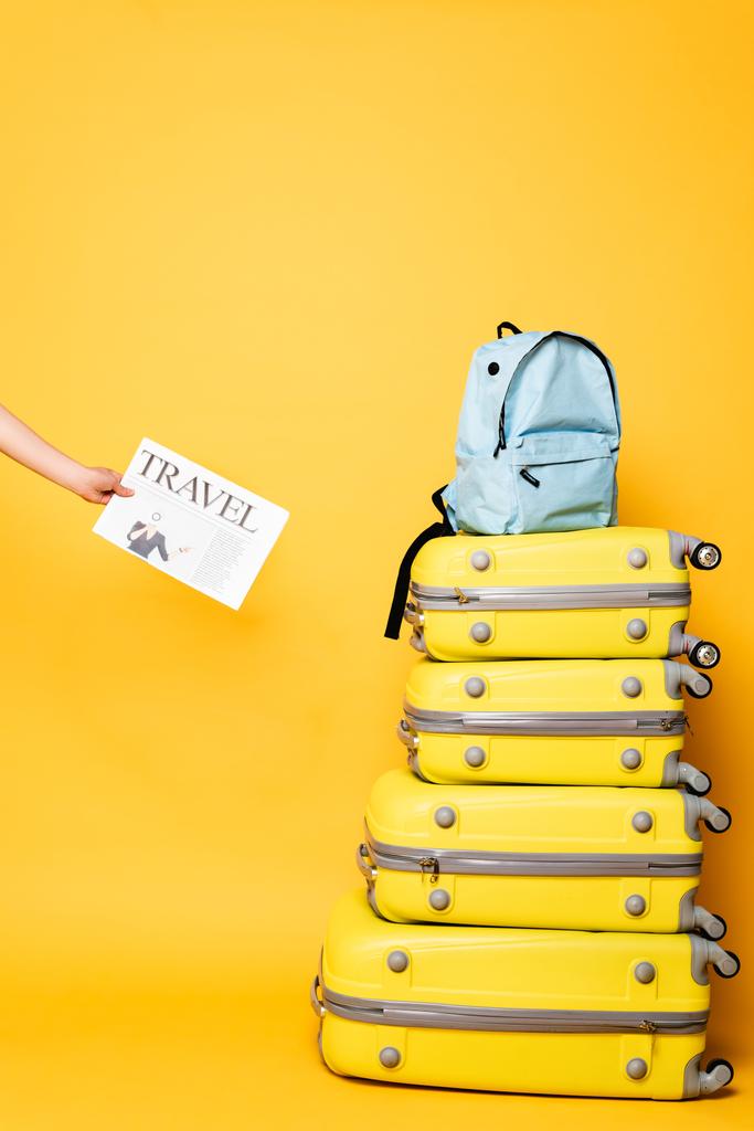 cropped view of woman holding travel newspaper near blue backpack on travel bags on yellow - Photo, Image
