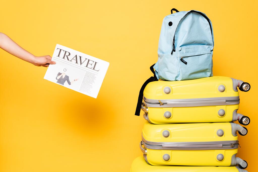przycięty widok kobiety trzymającej gazetę podróżną w pobliżu niebieskiego plecaka na torbach podróżnych na żółto - Zdjęcie, obraz
