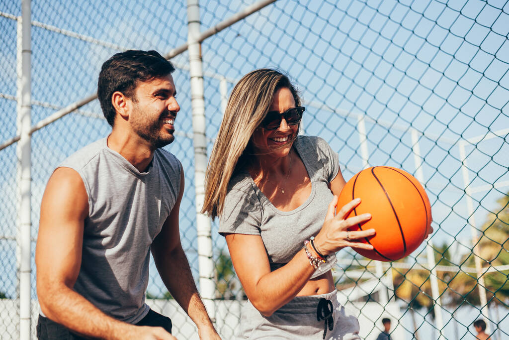 Ζευγάρι που διασκεδάζουν παίζοντας μπάσκετ έξω την ηλιόλουστη μέρα. - Φωτογραφία, εικόνα