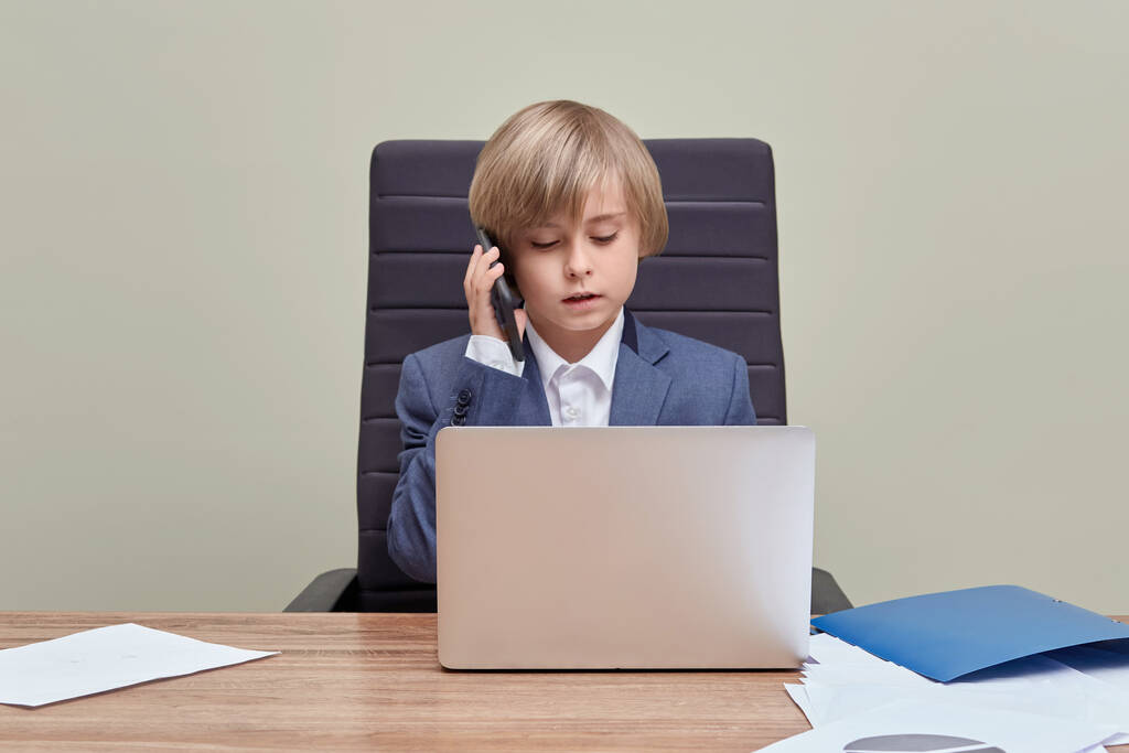 Der blonde Junge arbeitet im Büro mit einem Laptop und telefoniert. - Foto, Bild