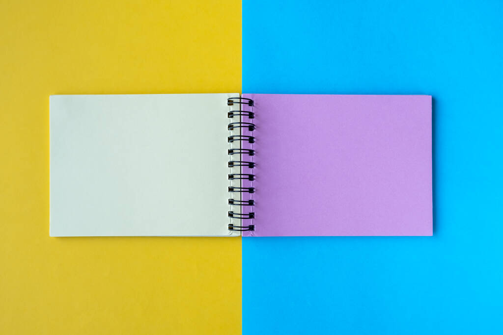 Un taccuino con pagine multicolori giace su uno sfondo giallo e blu. Vista dall'alto, disposizione piatta, spazio di copia. - Foto, immagini
