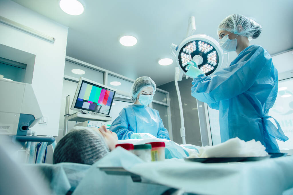 Професійний лікар стоїть поруч з пацієнтом і її колега дивиться на ліки в шприці
 - Фото, зображення
