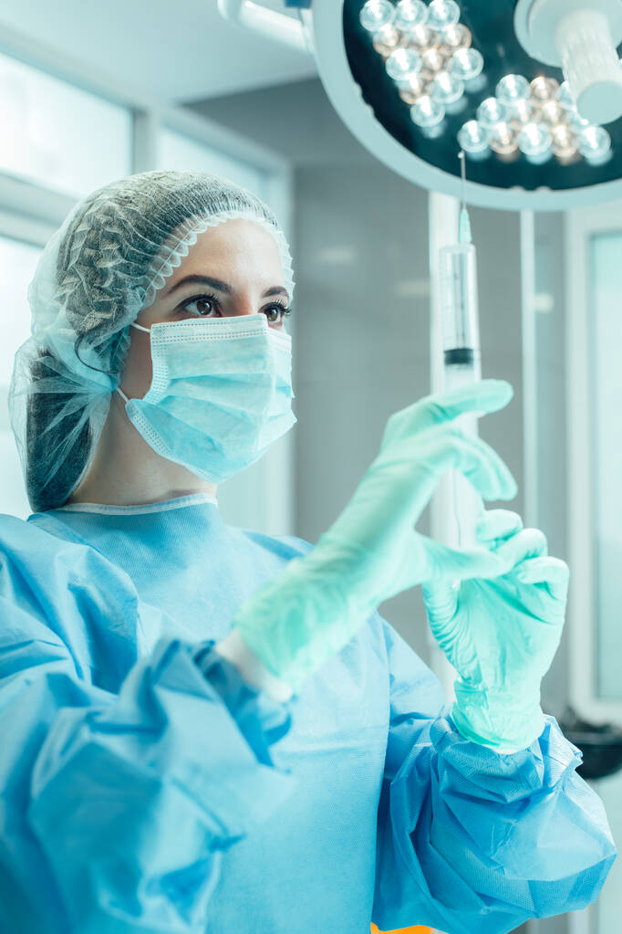 Professzionális orvosi dolgozó áll a műtőben fecskendővel a kezében és nézi. - Fotó, kép