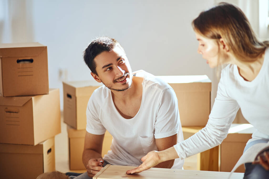 Couple assembling furniture in new home, moving boxes on background - Photo, Image