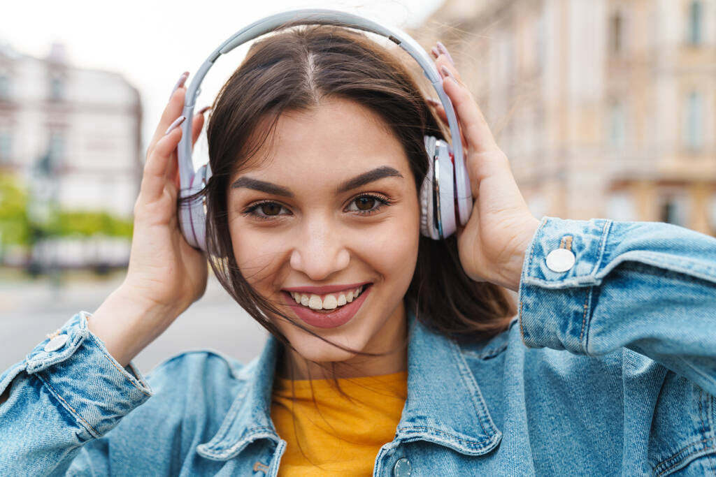 街の通りにワイヤレスヘッドフォンで音楽を聴きながら笑顔の素敵な喜びの女性のイメージ - 写真・画像