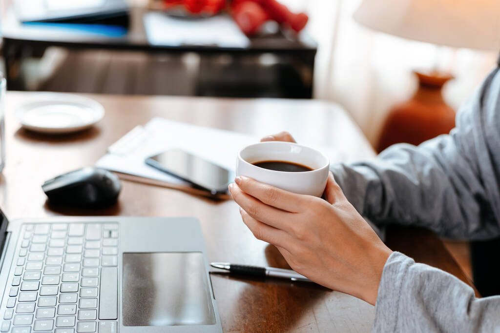 nő dolgozik laptop és tartsa csésze kávét, miközben ül a munkahelyen. - Fotó, kép