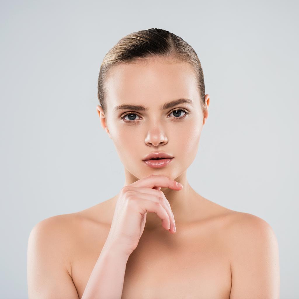 naked young woman looking at camera and touching face isolated on grey - Photo, Image