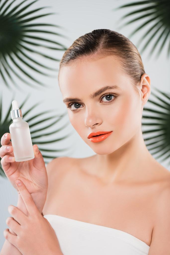 attractive woman holding bottle with serum near palm leaves on white - Photo, Image