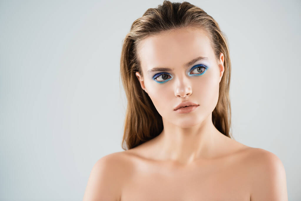γυμνή νεαρή γυναίκα με μπλε σκιά ματιών κοιτάζει μακριά απομονωμένη στο λευκό - Φωτογραφία, εικόνα