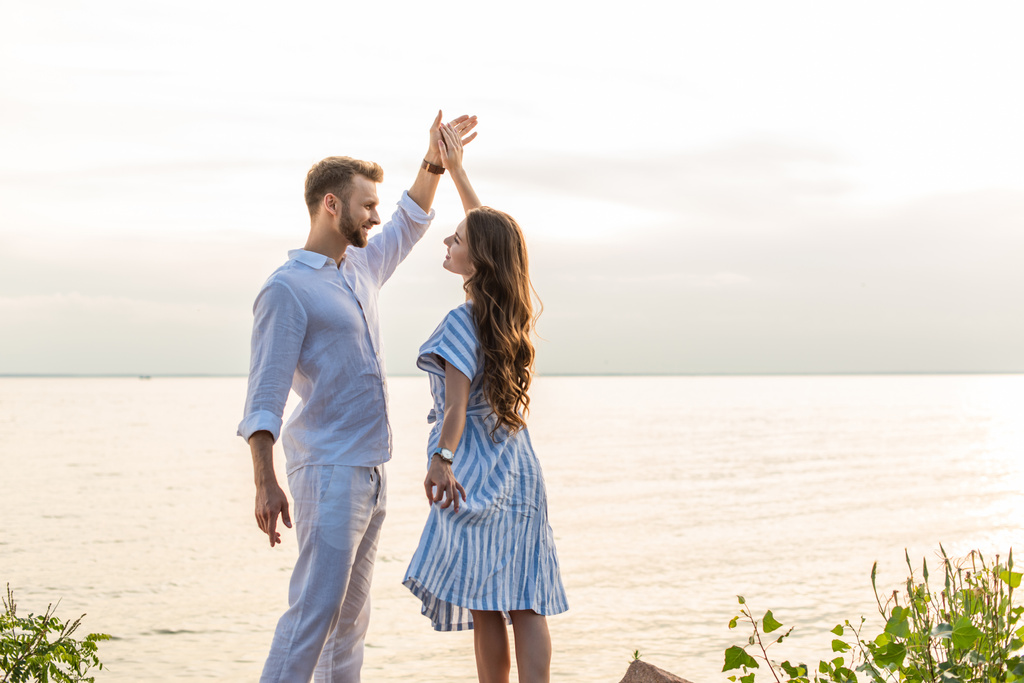 Fröhliches Paar hält Händchen und tanzt am See  - Foto, Bild