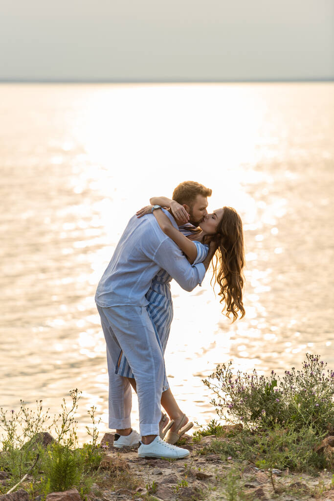 hombre guapo y atractiva mujer besándose cerca del lago
  - Foto, Imagen