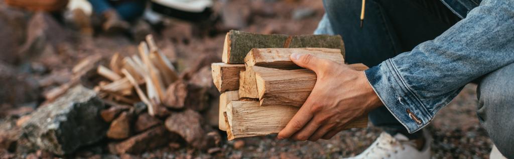 panoramic shot of man in denim jacket holding firewood in hands - Photo, Image
