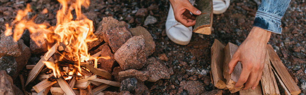 πανοραμική έννοια του ανθρώπου αγγίζοντας ξύλινο κούτσουρο κοντά καύση φωτιά - Φωτογραφία, εικόνα