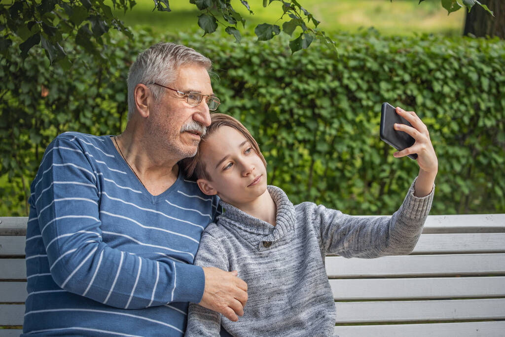 Bir çocuk ve büyükbabanın portresi, mutlu, neşeli büyükbaba ve torunlu akıllı telefon ile yaz parkında selfie çekiyor, boş zaman konsepti, okul tatili - Fotoğraf, Görsel