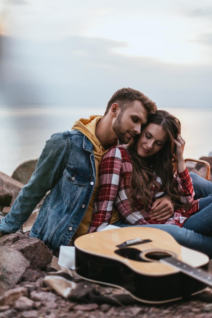 selective focus of happy couple with closed eyes sitting near acoustic guitar  - Photo, Image