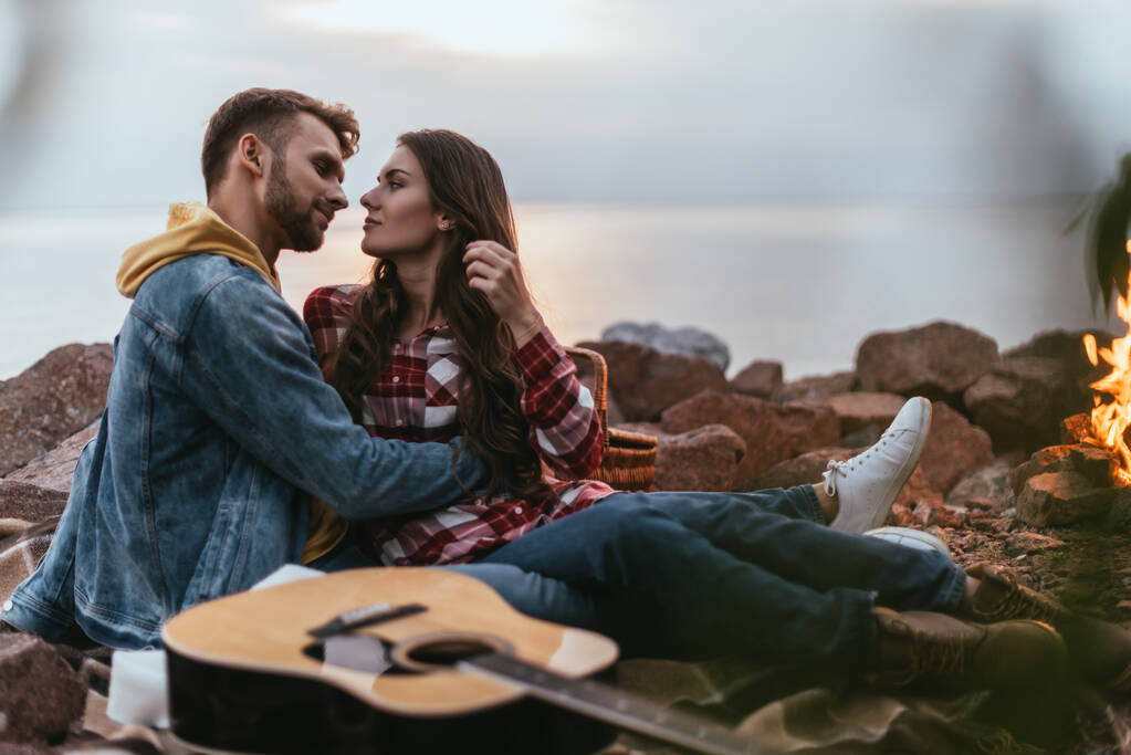 selektywny ostrość brodaty mężczyzna przytulanie dziewczyna w pobliżu gitara akustyczna i bonfire - Zdjęcie, obraz