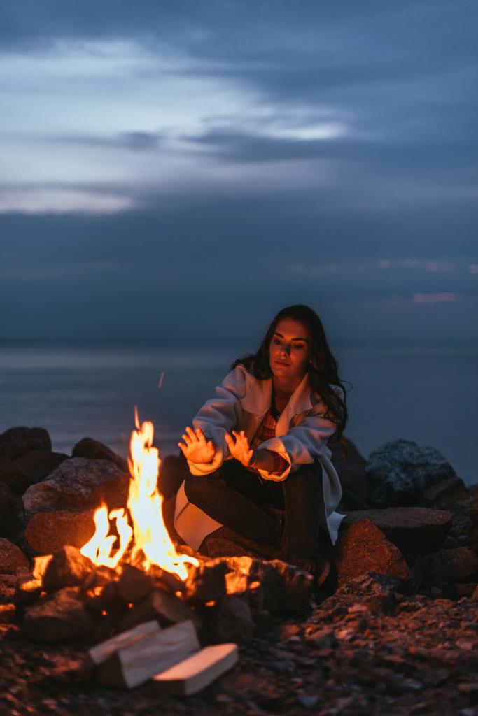 επιλεκτική εστίαση της γυναίκας να πάρει ζεστό κοντά στην καύση της φωτιάς τη νύχτα  - Φωτογραφία, εικόνα