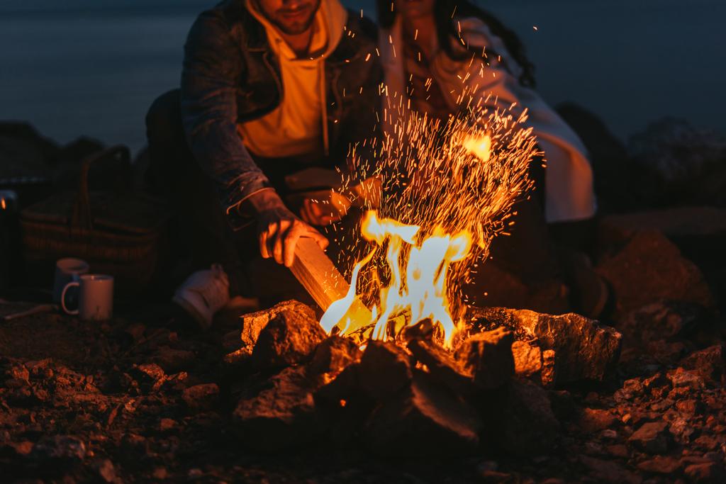 Ausgeschnittener Blick auf Mann, der Holzklotz in Lagerfeuer in der Nähe von Mädchen legt  - Foto, Bild