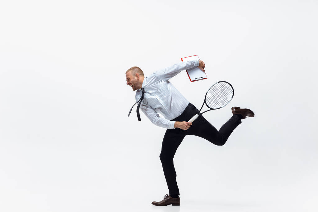 Время двигаться. Мужчина в офисной одежде играет в теннис на белом фоне студии. - Фото, изображение