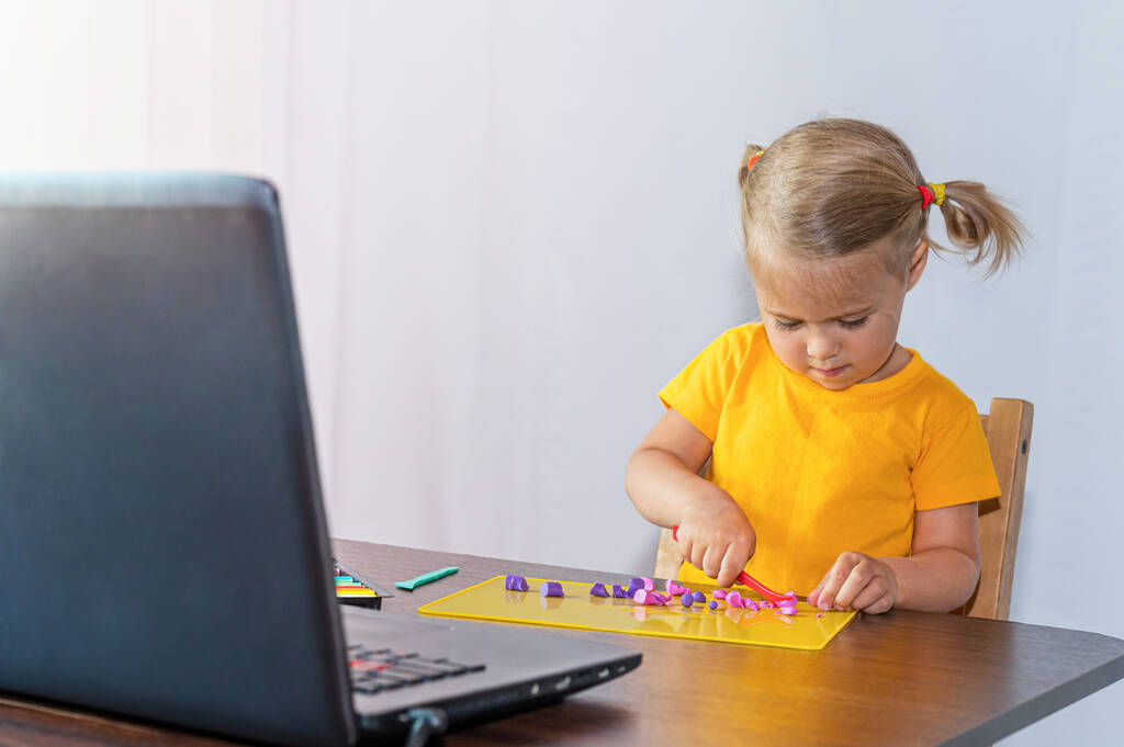 Un bambino fa la plastilina a casa, guardando una lezione su Internet. Educazione online. - Foto, immagini