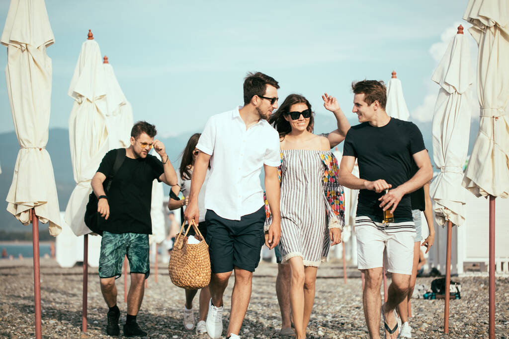 Vacanze, vacanze. gruppo di amici che si divertono sulla spiaggia, camminano, bevono birra, sorridono e si abbracciano - Foto, immagini