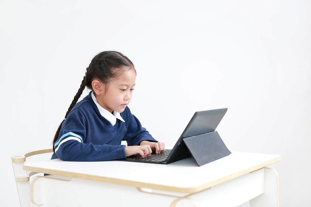 Portrait asiatique petite fille en uniforme scolaire à l'aide d'un ordinateur portable sur la table isolé sur fond blanc, Plan studio - Photo, image