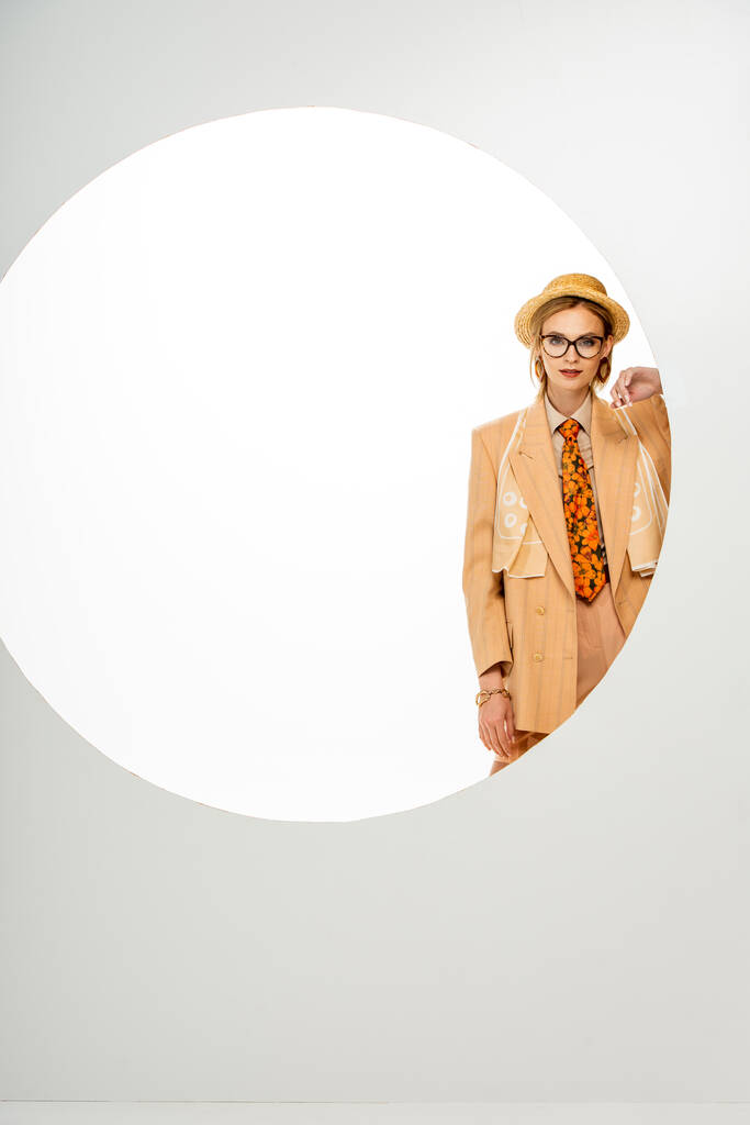 Hermosa chica en sombrero de paja y chaqueta beige mirando a la cámara al lado del círculo sobre fondo blanco
  - Foto, imagen