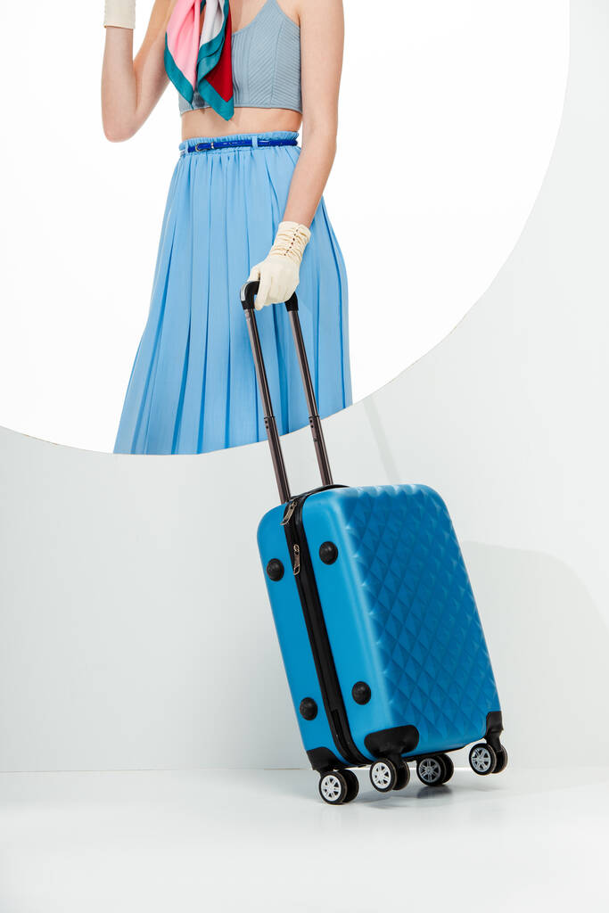 Gesneden weergave van stijlvol meisje met blauwe koffer achter ronde gat op witte achtergrond  - Foto, afbeelding