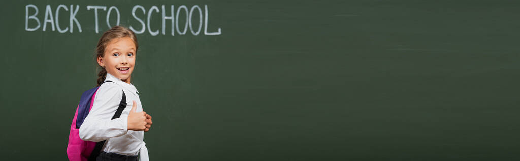 conceito horizontal de colegial feliz com mochila perto de quadro-negro com volta à inscrição da escola
 - Foto, Imagem