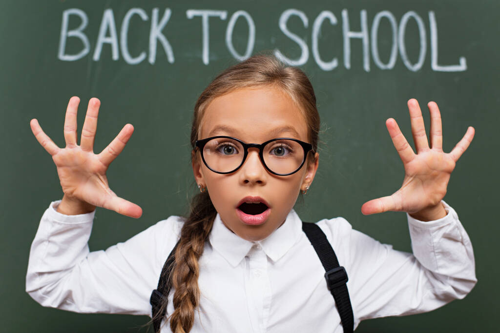 foyer sélectif de l'écolière dans les lunettes montrant geste effrayant près de tableau noir avec retour à l'école lettrage - Photo, image