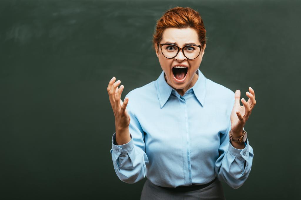 Злой учитель в очках жестикулирует и кричит возле доски - Фото, изображение