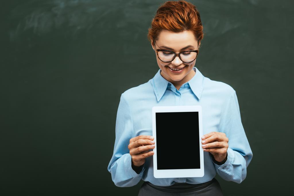 enseignant souriant tenant tablette numérique avec écran blanc tout en se tenant près du tableau - Photo, image