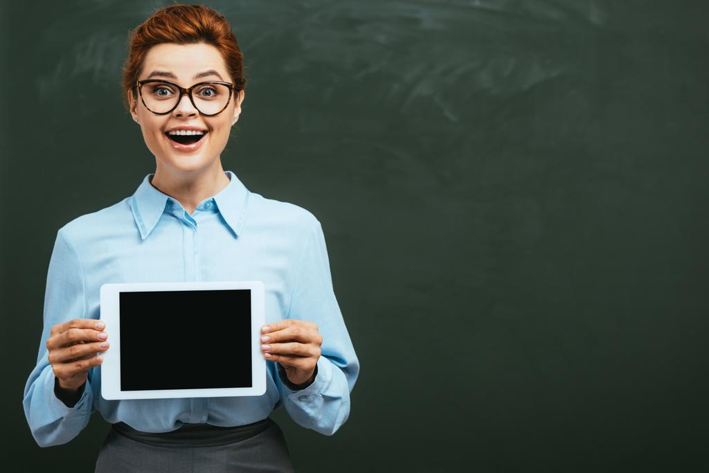excited teacher showing digital tablet with blank screen near chalkboard - Photo, Image