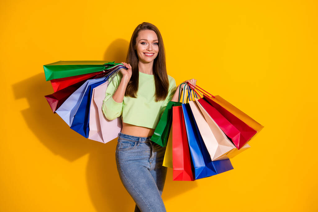 かなり魅力的なお店の女性の写真良い気分通りの外観は多くのショッピングバッグを保持緑のクロップドスウェットジーンズを着用孤立鮮やかな黄色の色の背景 - 写真・画像