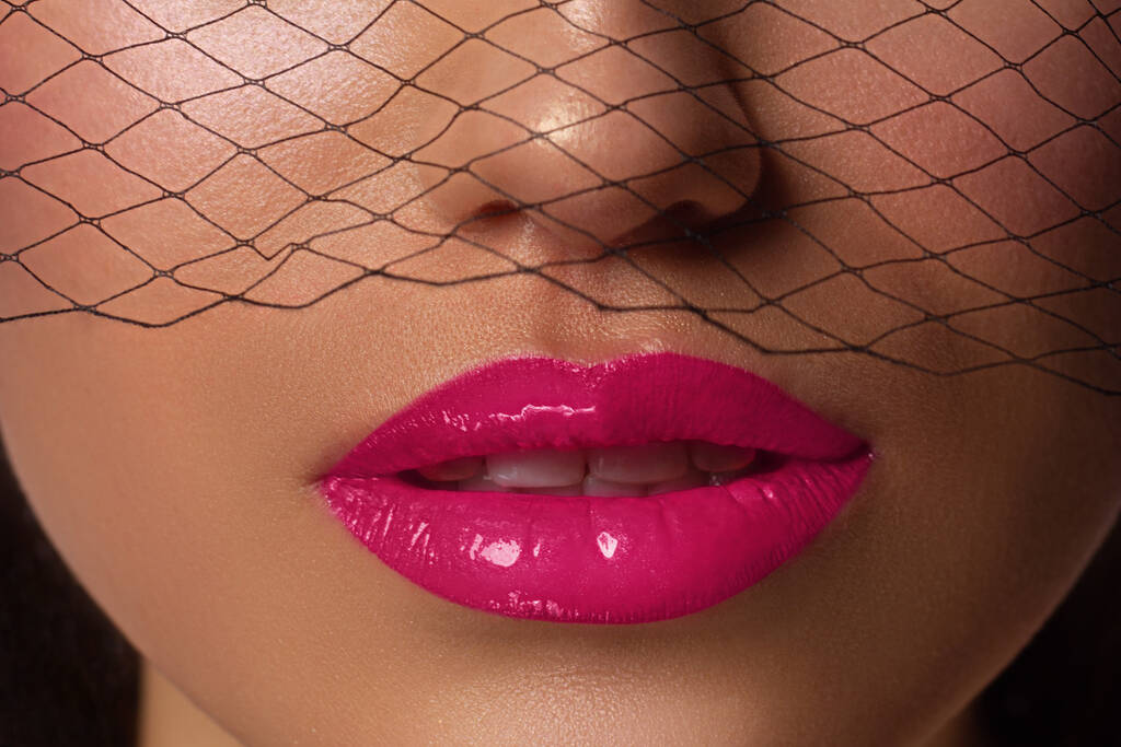 Κοντινό πλάνο των χειλιών της γυναίκας με fashion φωτεινό ροζ make-up. Όμορφο γυναικείο στόμα, γεμάτα χείλη με τέλειο μακιγιάζ. Μέρος του γυναικείου προσώπου. Επιλογή κραγιόν. Μαύρο πλέγμα μιας κούκλας Barbie - Φωτογραφία, εικόνα